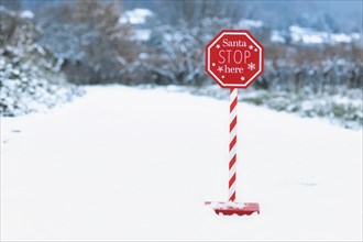 Red Christmas sign with text 'Santa Stop here' in snowy landscape