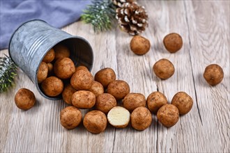German traditional Christmas sweets called Marzipankartoffeln. Round ball shaped almond paste pieces covered in cinnamon and cocoa powder spilling out of iron cup on wooden background