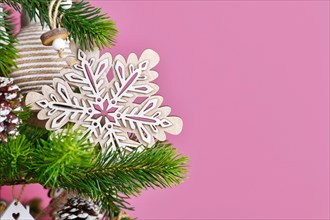Christmas tree branch with natural wooden snowflake ornament in front of pink background with copy space