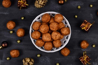 Traditional German Christmas sweets called Marzipankartoffeln. Round ball shaped almond paste pieces covered in cinnamon and cocoa powder in white bowl on dark background