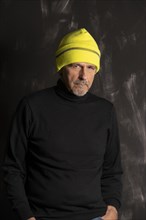 Elderly man with yellow winter cap scowls