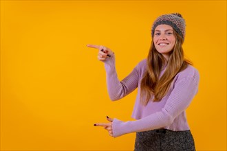 Woman in a woolen cap on a yellow background pointing to the left