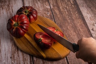 Close-up of a woman's hand with knife cutting tomatoes on a board on wooden table