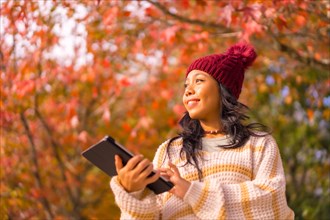 Asian girl in autumn with a tablet smiling in a forest of red leaves