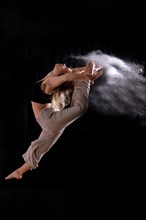 Young dancer performing a jump in studio photo session with a black background