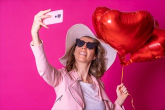 Blond caucasian woman having fun in a white hat and sunglasses in a nightclub with some heart balloons