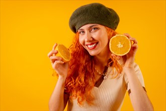 Redhead woman with an orange over isolated yellow background