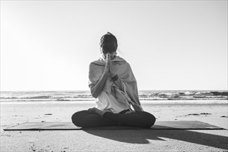 Portrait of a woman clasping hands while holding a japa mala at the beach. Namaste pose. Front view