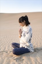 Side view of a woman clasping hands at the beach. Namaste pose