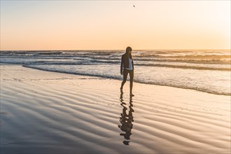 A lonely woman at the beach walking barefooted by the shore at sunrise. Copy space