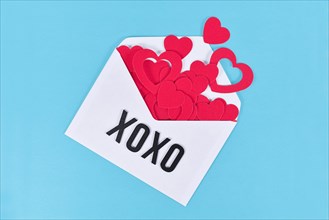 White love letter with hearts spilling out of it and letters XOXO on blue background