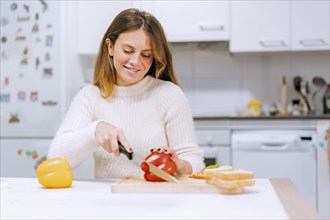 Vegetarian woman cooking a vegetable sandwich in the kitchen at home. cutting red pepper