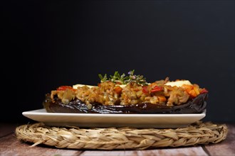 Eggplants stuffed with meat and vegetables on a white plate on a wooden table with a branch of rosemary in bloom