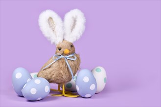 Easter chick with bunny ears and pastel Easter eggs on violet background