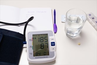 Blood pressure device notebook and pills on a white table