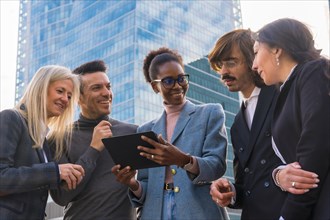 Group of smiling multi-ethnic business people looking at a tablet outside glass office building