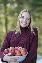 Portrait of a young blond woman holding a bowl of apples