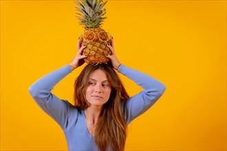 Woman with a pineapple in sunglasses in a studio on a yellow background