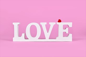White wooden word LOVE with red heart on pink background