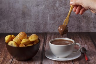 Woman spreading a sugared doughnut with a wooden fork on a hot chocolate in a white mug