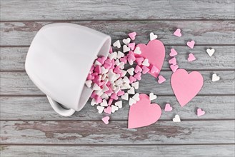 Pink and white sugar hearts spilling out of white tea cup on wooden background