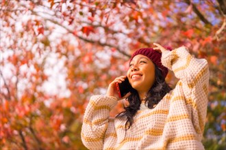 Portrait of an Asian woman in autumn with a mobile phone calling in a forest of red leaves