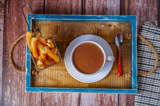Hot chocolate in a white mug with churros in a blue wooden tray on a wooden table