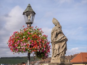 The flower-decorated streetlamp and the religious bridge statue of St. Fridericus on Alte Mainbruecke