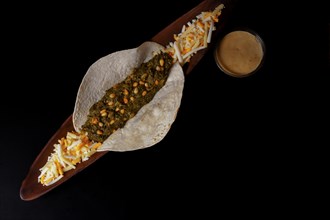 Taco with spinach and pine nuts bowl with cheese sauce and various types of cheeses as garnish and black background