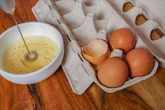 Beating an egg in a bowl with a small mixer with an egg cup at the bottom on a wooden table