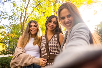 Women friends smiling in a park in autumn carefree taking a selfie