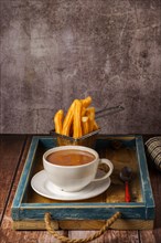 Hot chocolate in a white mug with churros in a blue wooden tray on a wooden table