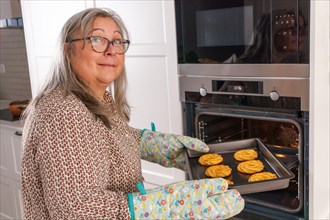 Older white-haired woman putting a tray of cookies in the oven