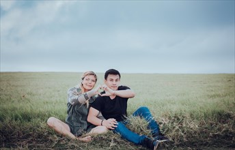 Couple sitting on the grass making a heart shape with their hands. Young couple in love in the field making heart shape. Lovers sitting in the field making a heart shape with their hands