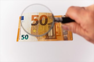 Fifty euro banknote seen with a magnifying glass on a white background and copy space