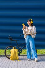Asian college girl listening to music with yellow headphones on a blue college background