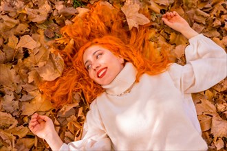 Red-haired girl lying on leaves in city park