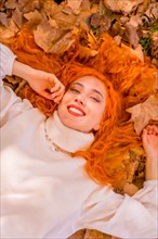 Redhead woman lying on leaves in city park smiling