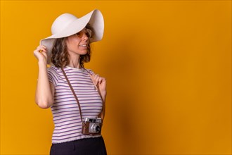 Caucasian girl in tourist concept with hat and photo camera on a yellow background