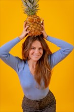 Portrait of a woman with a pineapple in sunglasses in a studio on a yellow background