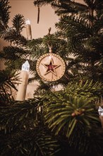 A wooden Christmas tree ball with a red star in the middle on a Christmas tree with Christmas tree lights
