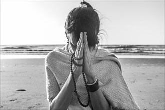 Portrait of a woman clasping hands while holding a japa mala at the beach. Namaste pose
