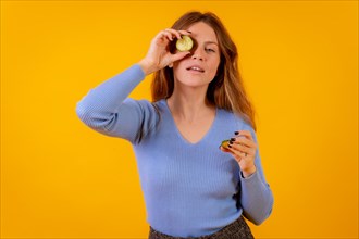 Vegan woman with a slice of cucumber on her eye on a yellow background