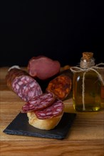 Tapa of iberian sausage on rustic bread with olive oil on a wooden board with black background