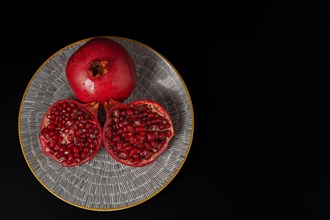 Fresh pomegranate opclose-up of fresh pomegranate opened on a yellow plate with black backgroundened on a plate with a black background