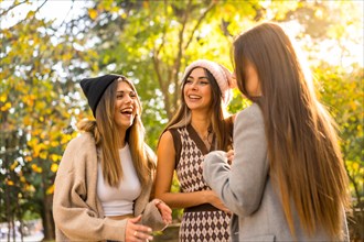 Women friends smiling in a park in autumn with woolen hats