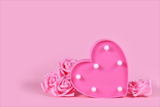 Valentine's day composition with roses and heart shaped lamp on pink background with copy space