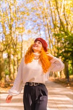 Red-haired woman in a beret walking through a city forest park at sunset