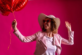 A caucasian woman enjoying dancing with a white hat in a nightclub with some heart balloons