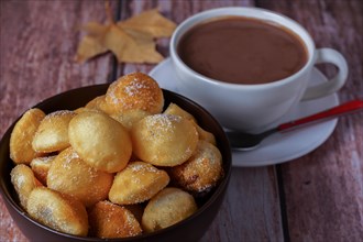 Homemade doughnuts with sugar in a bowl and hot chocolate in a white mug on a wooden table